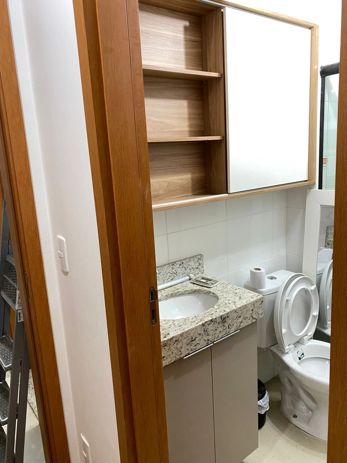 Banheiro Compacto e Funcional: Ambiente com design moderno, utilizando granito e madeira clara. Cores neutras criam harmonia, enquanto os armários otimizam o espaço. Destaque para a praticidade e funcionalidade.